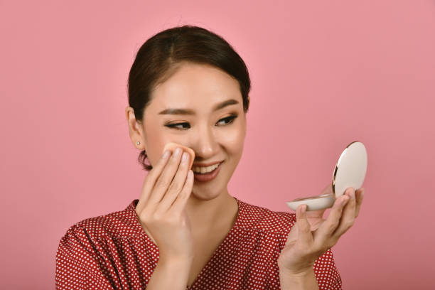 asian woman applying makeup cosmetics while looking at the mirror, midday face powder foundation touch up to keep looking fresh, removing excess greasy oil. - face powder imagens e fotografias de stock