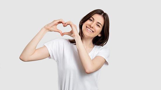 Love sign. Compassion support. Happy woman showing heart gesture isolated on neutral background.