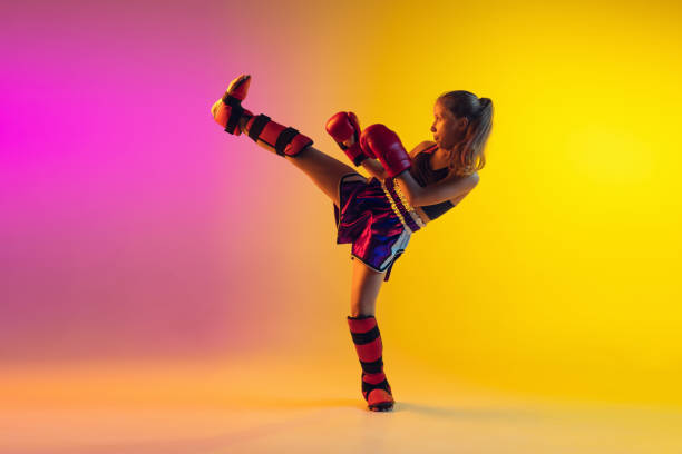 Little caucasian girl, kick boxer on gradient background in neon light, active and expressive. Concept of motion, action, motivation, childhood. Training winner, emotional. Sales, ad, copyspace.
