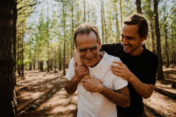 père et fils adulte étreignant et riant ensemble dans les bois après une course - beautiful caucasian teenager running photos et images de collection