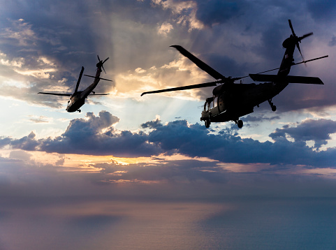 Black Hawk Military Helicopters flying over sea at sunset