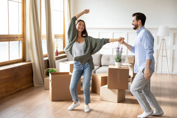 Happy young wife and husband dancing, celebrating moving day Happy young wife and husband dancing in modern living room with cardboard boxes with belongings, excited family celebrating moving day, satisfied customers relocating into new apartment, mortgage couple relationship stock pictures, royalty-free photos & images