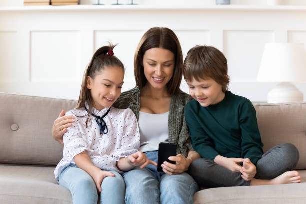 istock Smiling young mother with children using smartphone, sitting on couch 1251287053