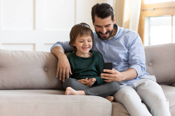 istock Happy father with little son using smartphone, sitting on couch 1251287073