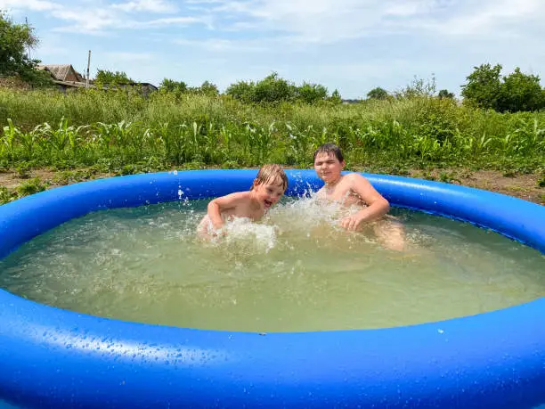 Two fair-skinned children bathe in an inflatable pool on a summer cottage in the summer. Free space. Defocus light background. Active lifestyle concept.