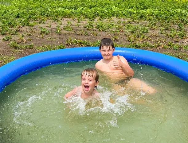 Two fair-skinned children bathe in an inflatable pool on a summer cottage in the summer. Free space. Defocus light background. Active lifestyle concept.