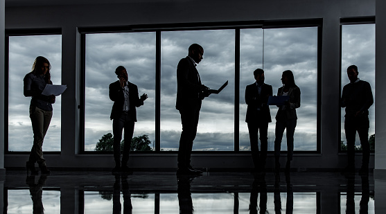 Large group of multi-tasking business people working in a dark hallway of an office building.