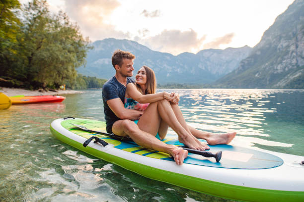 couple in early 30s sitting together on paddleboard - sport exercising men julian alps imagens e fotografias de stock