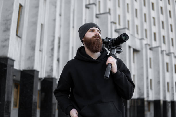 istock Bearded Professional videographer in black hoodie holding professional camera on 3-axis gimbal stabilizer. Filmmaker making a great video with a professional cinema camera. Cinematographer. 1251297761