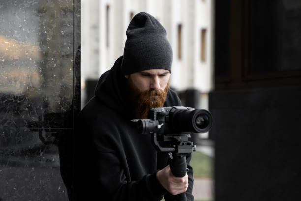 istock Bearded Professional videographer in black hoodie holding professional camera on 3-axis gimbal stabilizer. Filmmaker making a great video with a professional cinema camera. Cinematographer. 1251299389