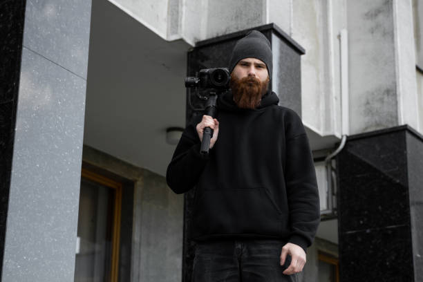 istock Bearded Professional videographer in black hoodie holding professional camera on 3-axis gimbal stabilizer. Filmmaker making a great video with a professional cinema camera. Cinematographer. 1251299693