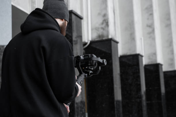 Bearded Professional videographer in black hoodie holding professional camera on 3-axis gimbal stabilizer. Filmmaker making a great video with a professional cinema camera. Cinematographer.