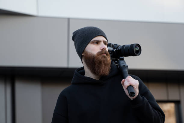 istock Bearded Professional videographer in black hoodie holding professional camera on 3-axis gimbal stabilizer. Filmmaker making a great video with a professional cinema camera. Cinematographer. 1251301810