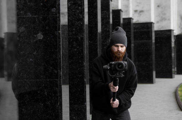 istock Bearded Professional videographer in black hoodie holding professional camera on 3-axis gimbal stabilizer. Filmmaker making a great video with a professional cinema camera. Cinematographer. 1251303830