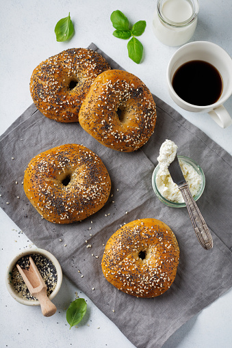 Variety fresh whole-grain bagels with poppy seeds, sesame seeds and ingredients for breakfast  on a light concrete or stone background. Selective focus. Top view. Copy space.