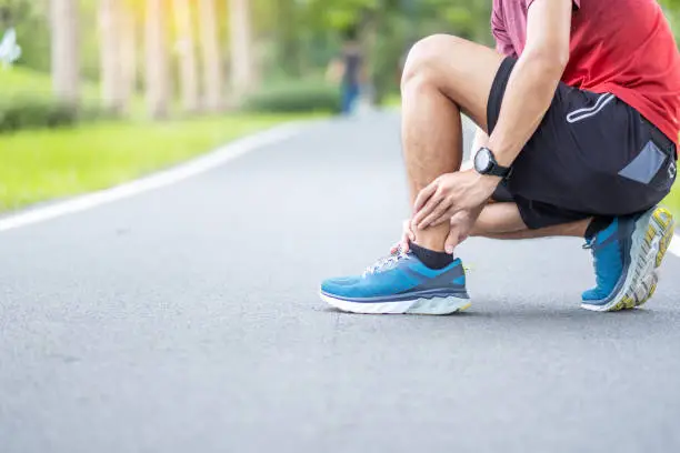 Young adult male with his muscle pain during running. runner man having leg ache due to Ankle Sprains or Achilles Tendonitis. Sports injuries and medical concept