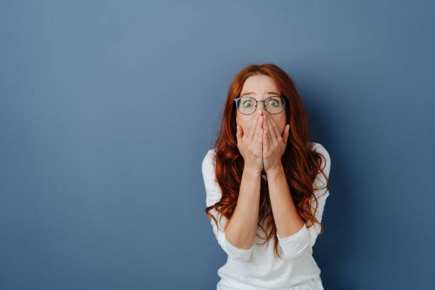 istock Terrified young woman with hands to mouth 1251305426