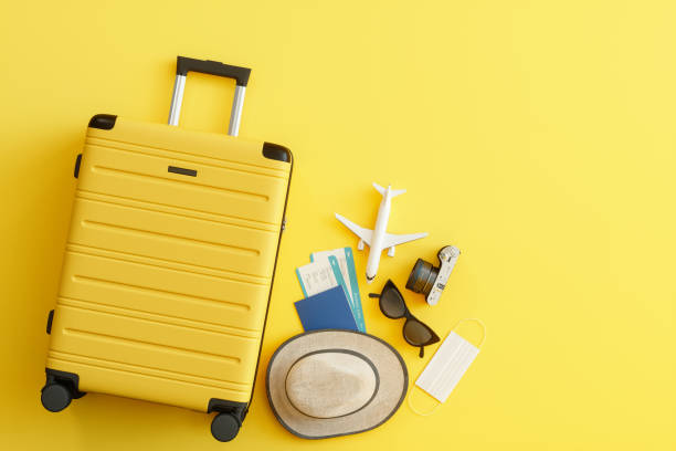 máscara médica, maleta con sombrero de sol, cámara, pasaporte, billete de avión, gafas de sol y avión sobre fondo amarillo - turismo vacaciones fotografías e imágenes de stock