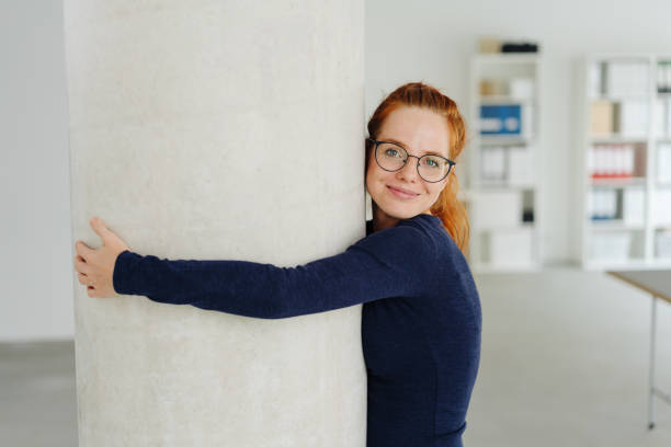istock Smiling young woman at the office hugging a pillar 1251306012