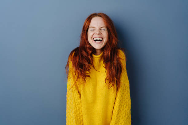 Quirky young woman screwing up her eyes Quirky young woman screwing up her eyes as she enjoys a hearty laugh at a joke over a blue studio background with copy space offbeat stock pictures, royalty-free photos & images