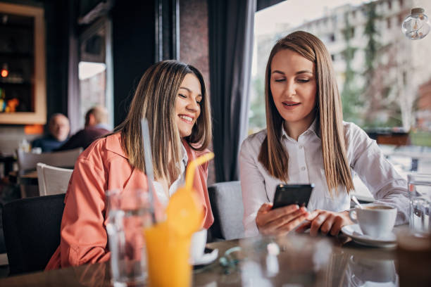istock Two young ladies sitting in cafe and using smart phone 1251307504