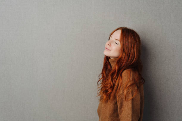 Blissful serene young woman with closed eyes tilting her head back with a quiet smile of pleasure as she takes a moment to relax over a grey studio background with copy space