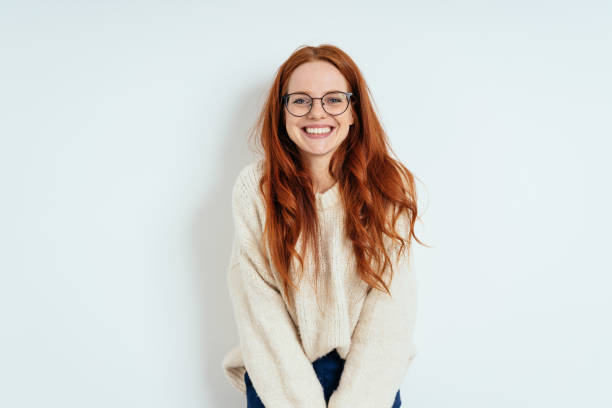 Smiling friendly young woman wearing spectacles Smiling friendly young woman with long red hair wearing spectacles looking at the camera with a vivacious smile against a white interior wall with copy space smiling stock pictures, royalty-free photos & images