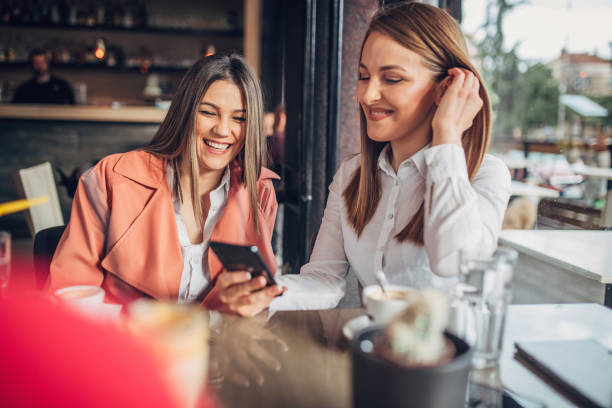 istock Two young ladies sitting in cafe and using smart phone 1251309092