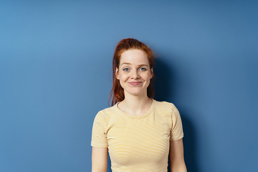 Pert young woman with a gleeful grin looking at the camera on a blue studio background with copy space