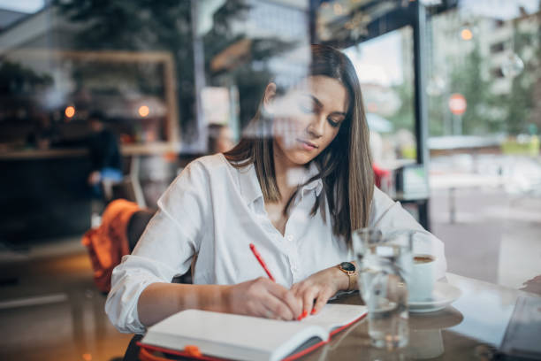istock Woman author sitting in cafe and writing notes in notebook 1251310060