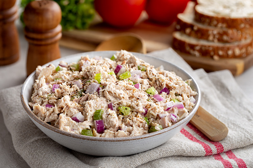 Tuna salad in a bowl on a napkin with makings for sandwiches in background