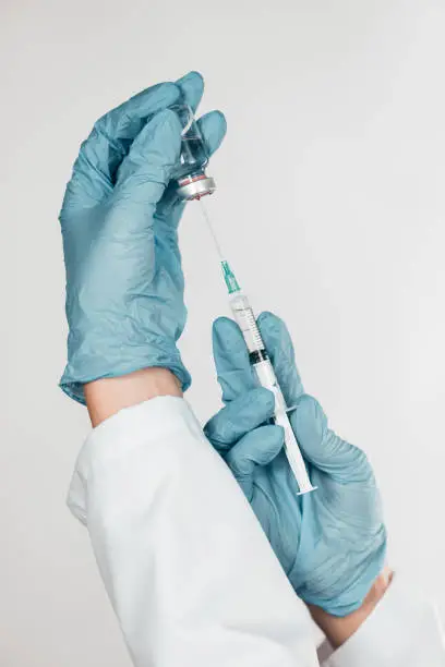 Hands in gloves holding syringe and liquid drug or a vaccine.