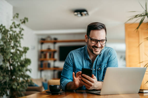 Portrait of a happy man with smart phone and laptop, indoors. Portrait of a happy man with smart phone and laptop, indoors. house phone stock pictures, royalty-free photos & images