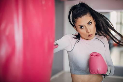One fit young woman with boxing gloves punching a punching bag in the gym.