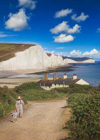 Eastbourne, England - July 18, 2020: A tourist walks there on the magnificent white cliffs known as Seven Sisters at low tide, Eastbourne, East Sussex, England.

Square panoramic.