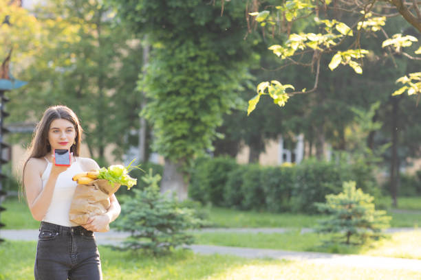 istock Happy girl using a smart phone voice recognition audio ai message speech function on line walking on a park background and carrying bag with food 1251321292