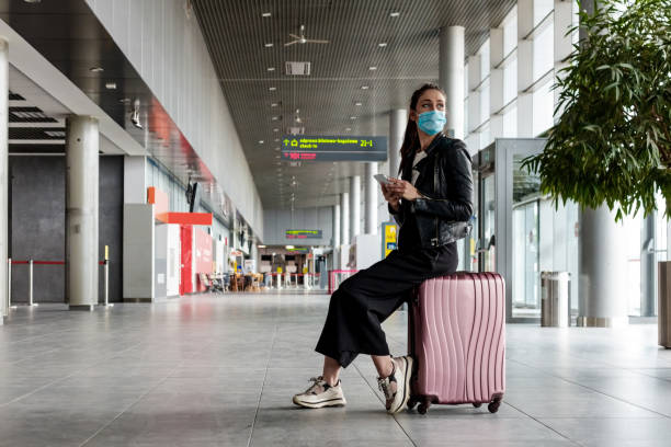 在機場攜帶行李的年輕女子,戴著n95面罩 - 乘客 圖片 個照片及圖片檔