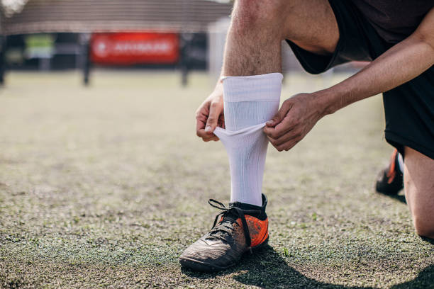 calciatore maschio che fissa il calzino sul campo da calcio - soccer socks foto e immagini stock