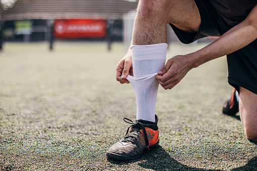 Male soccer player fixing his sock on soccer field, preparing for match.