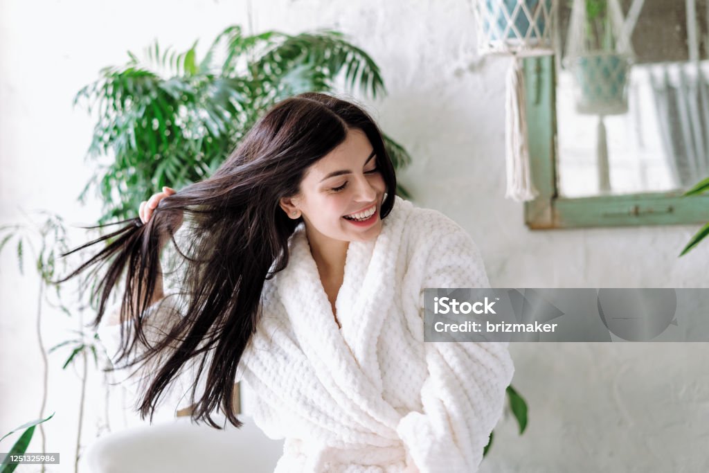 Young adult female spending free time at home Smiling woman shaking head with floating hair, laughing wide, having fun at home. Happy young adult female in bathrobe spending morning at bathroom Hair Stock Photo