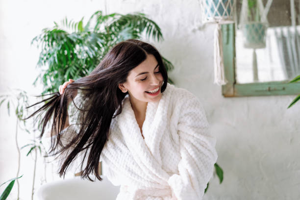 Young adult female spending free time at home Smiling woman shaking head with floating hair, laughing wide, having fun at home. Happy young adult female in bathrobe spending morning at bathroom shampoo stock pictures, royalty-free photos & images