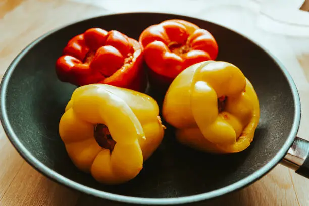Colorful yellow and red sweet peppers stuffed with savory ground meat ready for cooking in a frying pan in close up