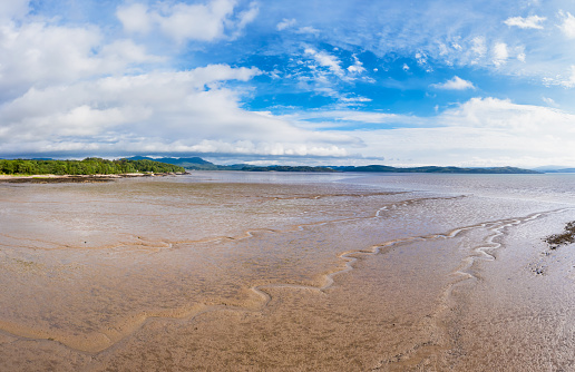 The view on a bright sunny summer day across Auchencairn Bay. The location is in Dumfries and Galloway south west Scotland. Beyond the bay is the Solway Firth, a stretch of water between the north west coast of England and the south west coast of Scotland.\nThe image was created by merging images captured by a drone flying at a low altitude.