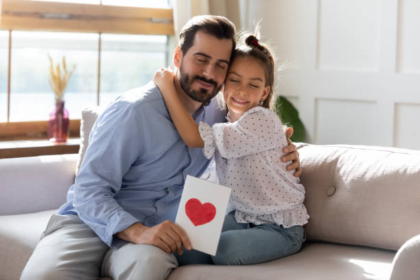 istock Pretty girl congratulating father, hugging, presenting greeting card 1251332370