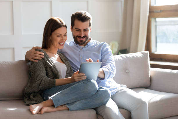Happy young couple using computer tablet together, sitting on couch