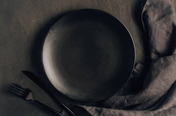 istock Black table setting: plate, napkin, silverware on black wooden background 1251338537