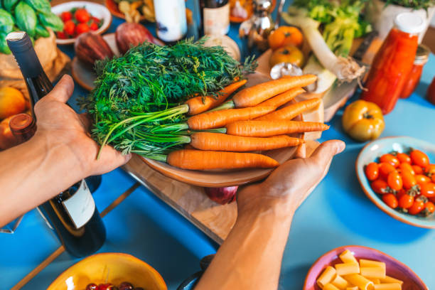 Hands holding carrots dish from above\nBackground table filled with large variety of food