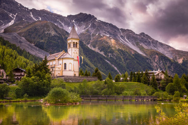 церковь на озере и деревне над идиллическим пейзажем итальянских альп, сулден, недалеко от пассо-делло-стельвио, италия - sulden стоковые фото и изображения