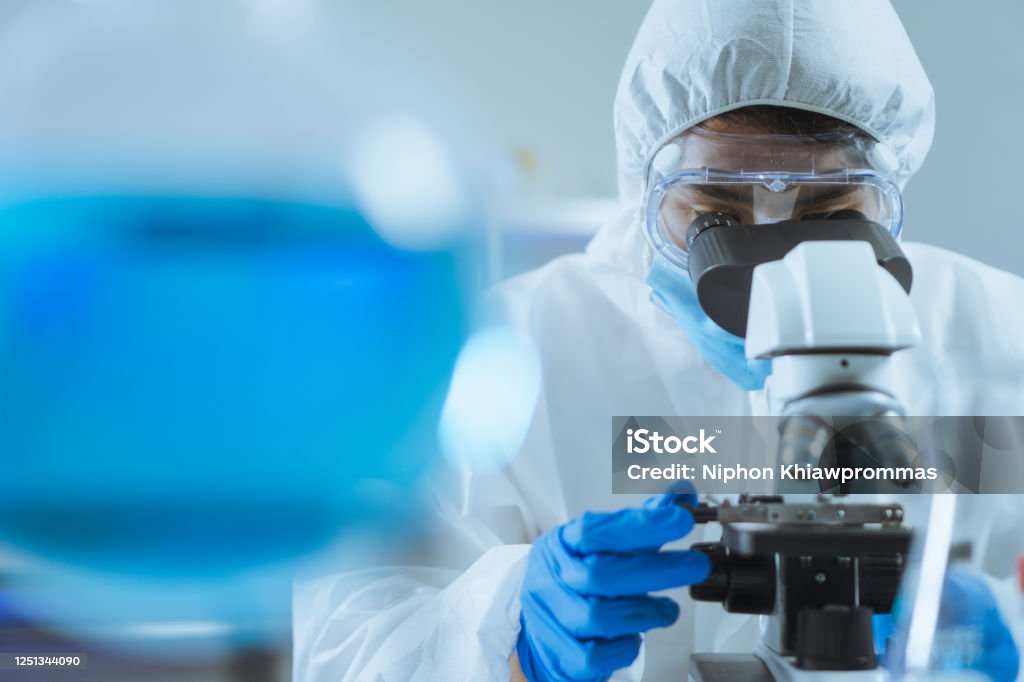若いアジアのハンサムな男の科学者は、焦点を調整し、実験室で生化学的な細胞を見て顕微鏡を使用しています.コロナウイルスの実験室パンデミックで医師と科学者の仕事, COVID19概念 - 実験室のロイヤリティフリーストックフォト