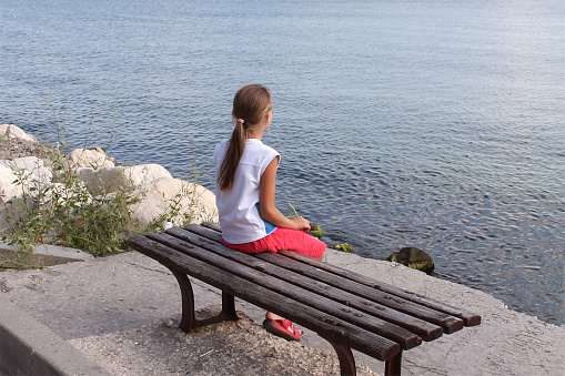 the girl dreamily looks at the sunset sitting on a bench by the sea